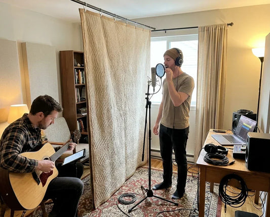 Homemade recording studio with a singer and guitarist recording beside a DIY comforter sound barrier.