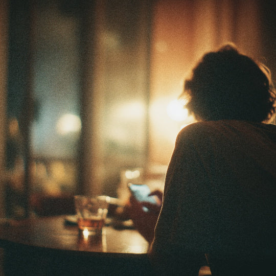 Person sitting at a bar counter with a drink, backlit by warm light