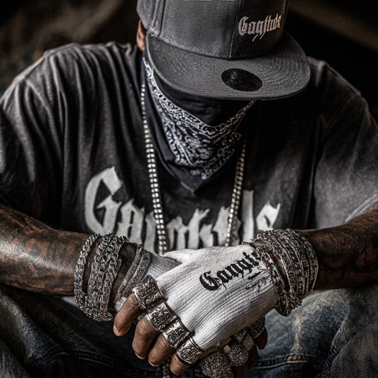 Person wearing a 'Gangsta' t-shirt, cap, and gloves with tattoos in an urban setting.