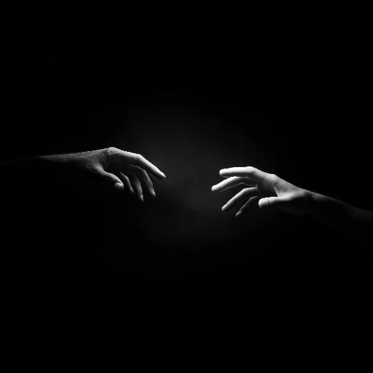 Black and white image of two hands reaching towards each other against a dark background