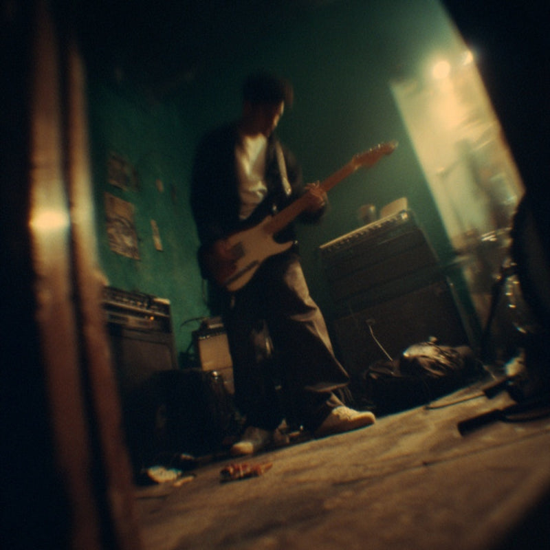 Person playing guitar in a dimly lit room with musical equipment.