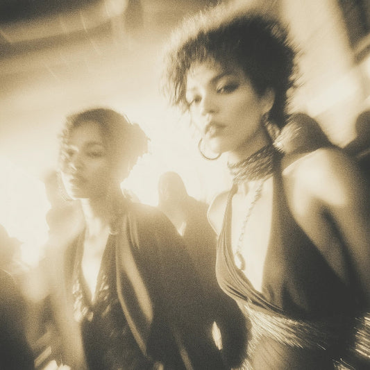 Two women in formal attire standing close together with a warm glow.