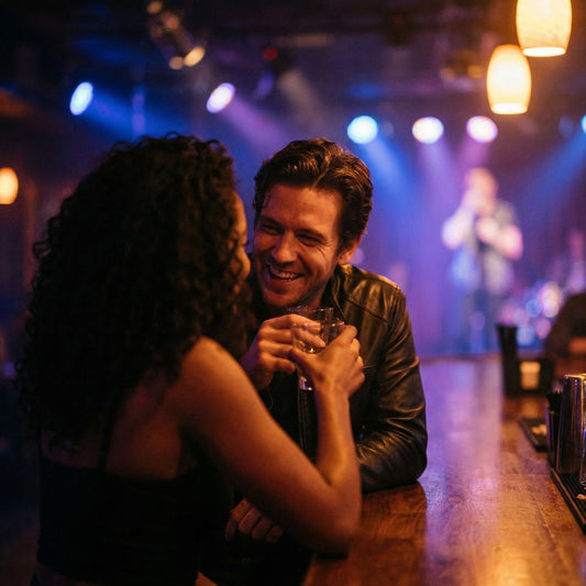 Two people sitting at a bar, engaged in conversation with dim lighting and colorful lights in the background.