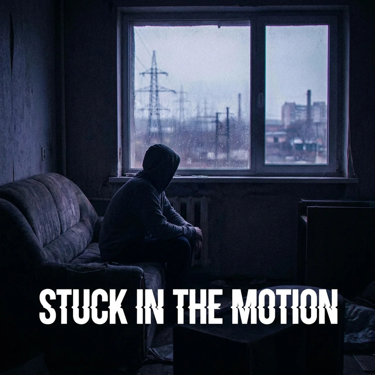 A dark, moody scene of a person in a hoodie sitting on a worn couch in a dim room, facing a large window with an industrial cityscape and power lines outside. Large white text at the bottom reads 'STUCK IN THE MOTION'.