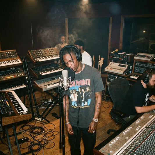 Person in a recording studio with musical equipment and another person in the background.